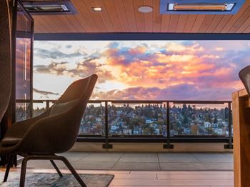 A chair is in the foreground of a room with a view of a cityscape at sunset.